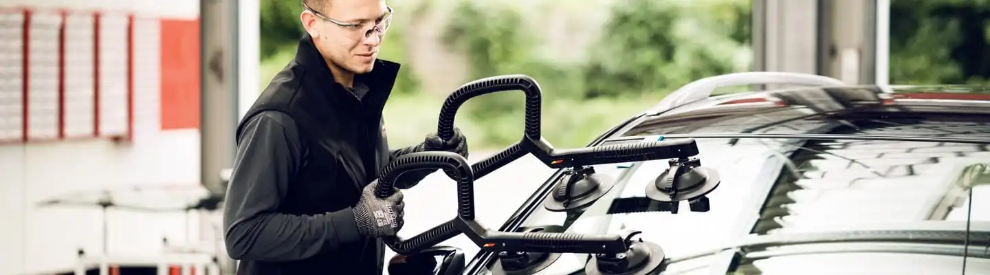 Monteur setzt mit Gerät neue Frontscheibe in Auto ein