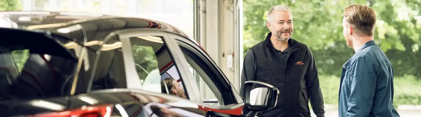 Kunde und Monteur stehen neben einem Auto und reden