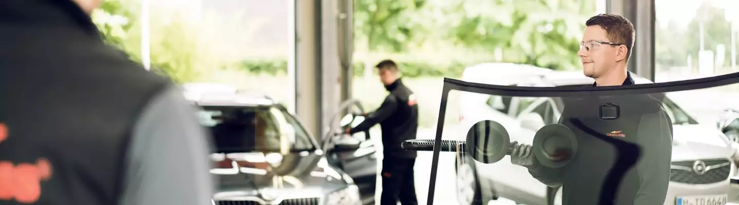 Ein Monteur, der eine Windschutzscheibe zum Auto trägt
