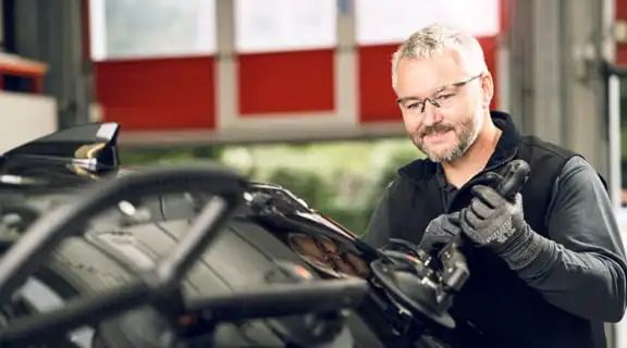 Monteur steht am Auto und richtet eine Heckscheibe aus um diese in das Auto einzusetzen
