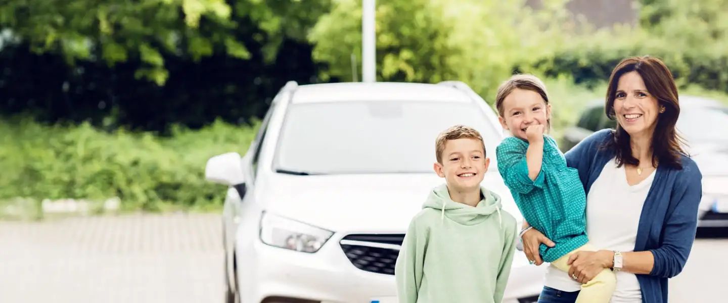 Frau mit zwei Kindern steht vor einem Auto im Freien