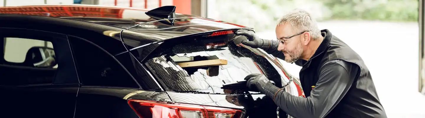 Monteur arbeitet an durchgeschlagener Heckscheibe eines Autos